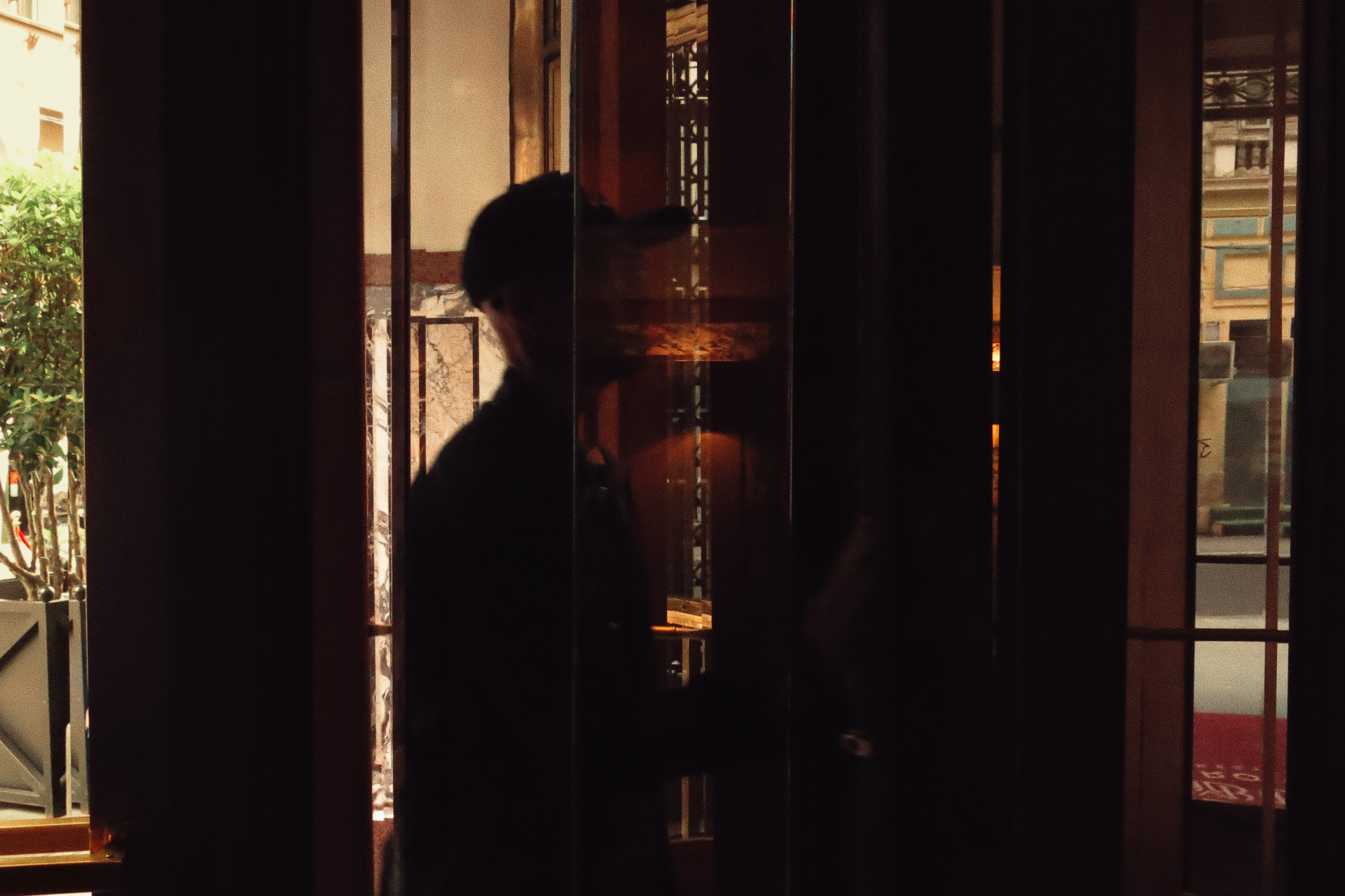Silhouette of a man in a cap behind reflective glass doors with a Parisian street view