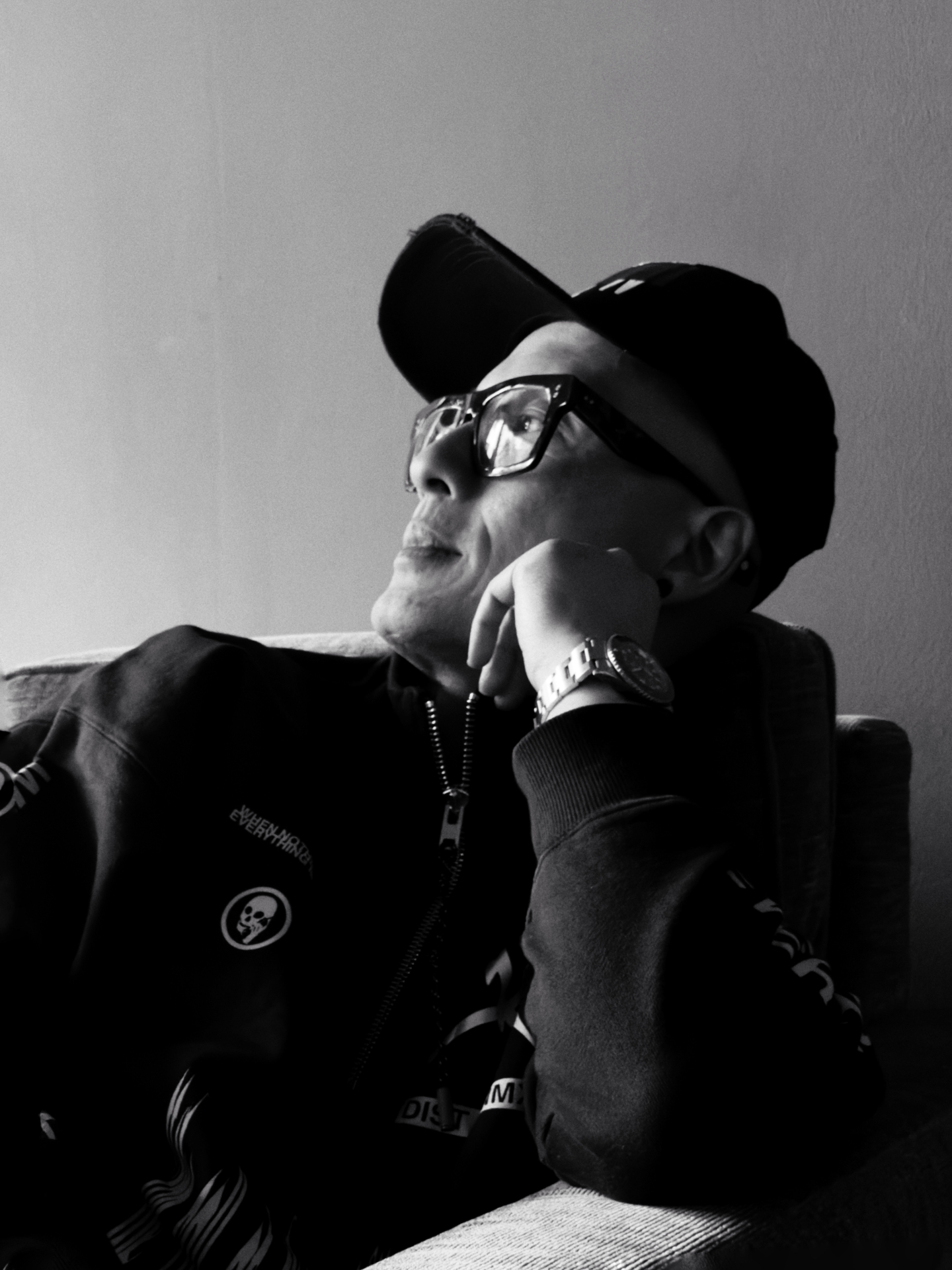 Black and white portrait of a man in a cap and glasses, resting his chin on his hand